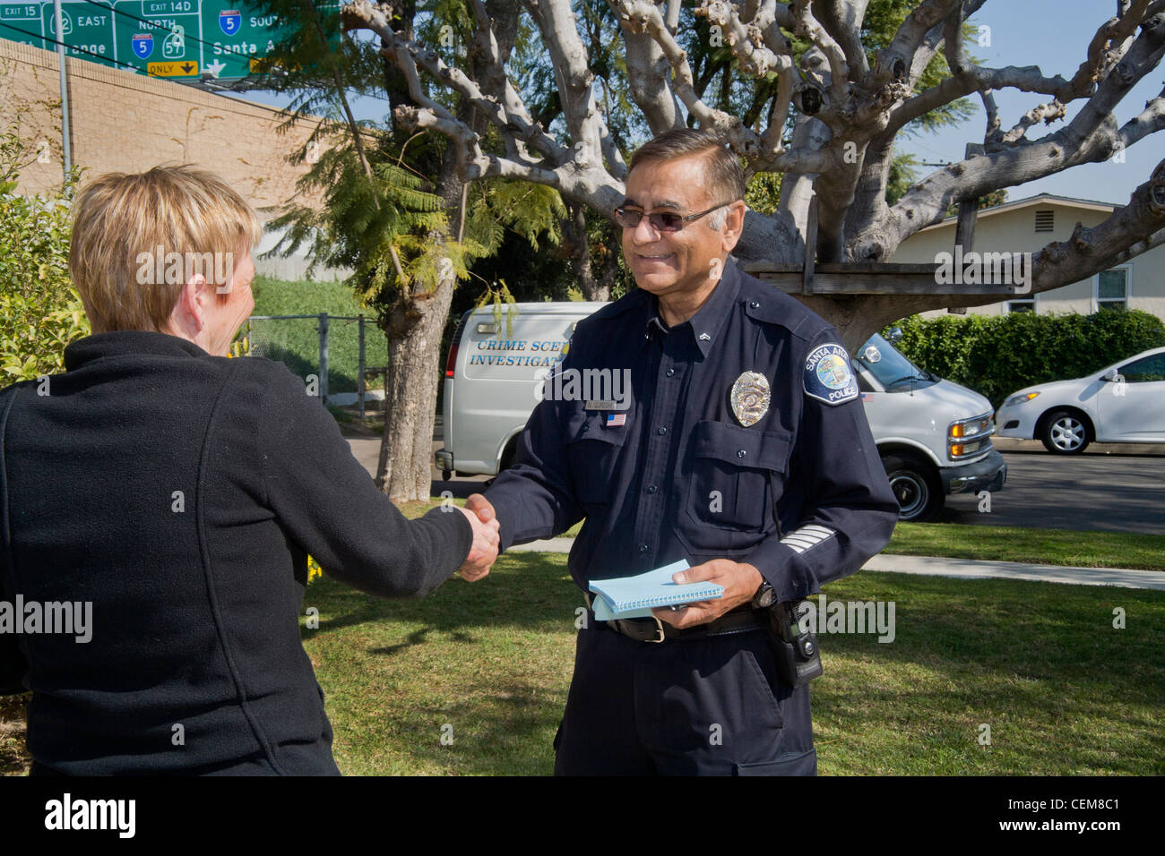 A Pakistani-American police crime scene investigator shakes hands with a homeowner after collecting evidence after a break-in. Stock Photo