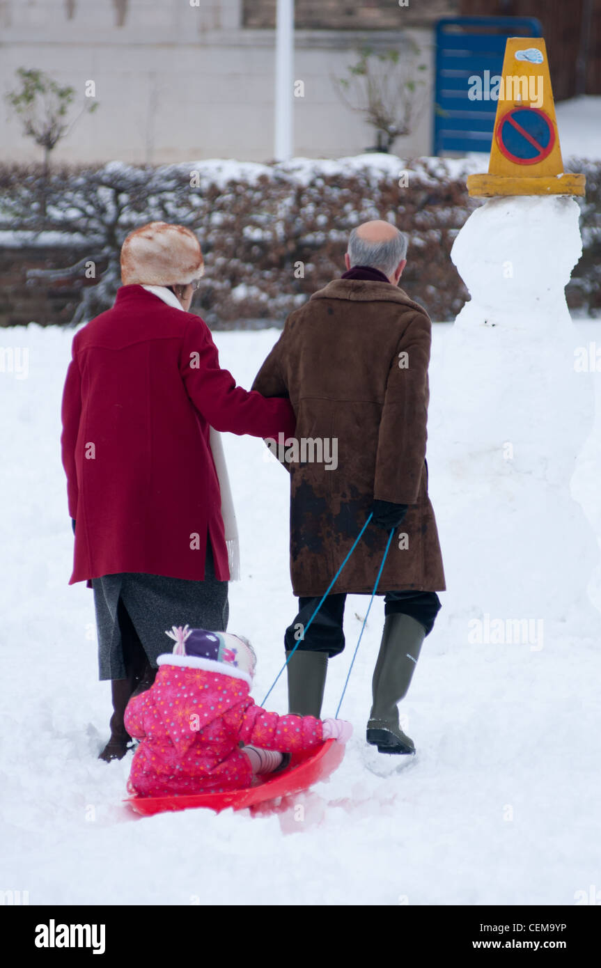 An old couple pull their grand daughter in winter snow in Cambridge, England. Stock Photo