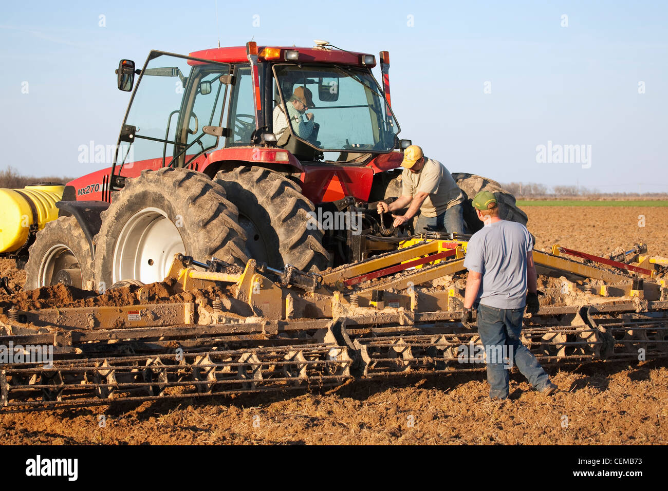 Three farmers work to set up a secondary tillage implement during field preparation operations prior to planting cotton / USA. Stock Photo