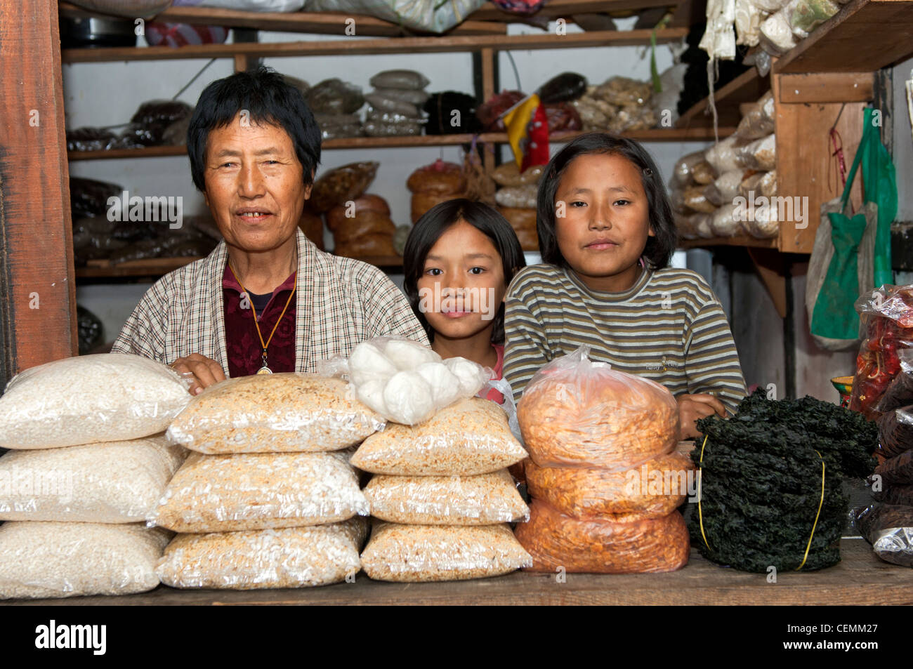 Woman with her two daughters behind rice bags looking out of their market stall at vegetable market in Lobesa, Bhutan Stock Photo