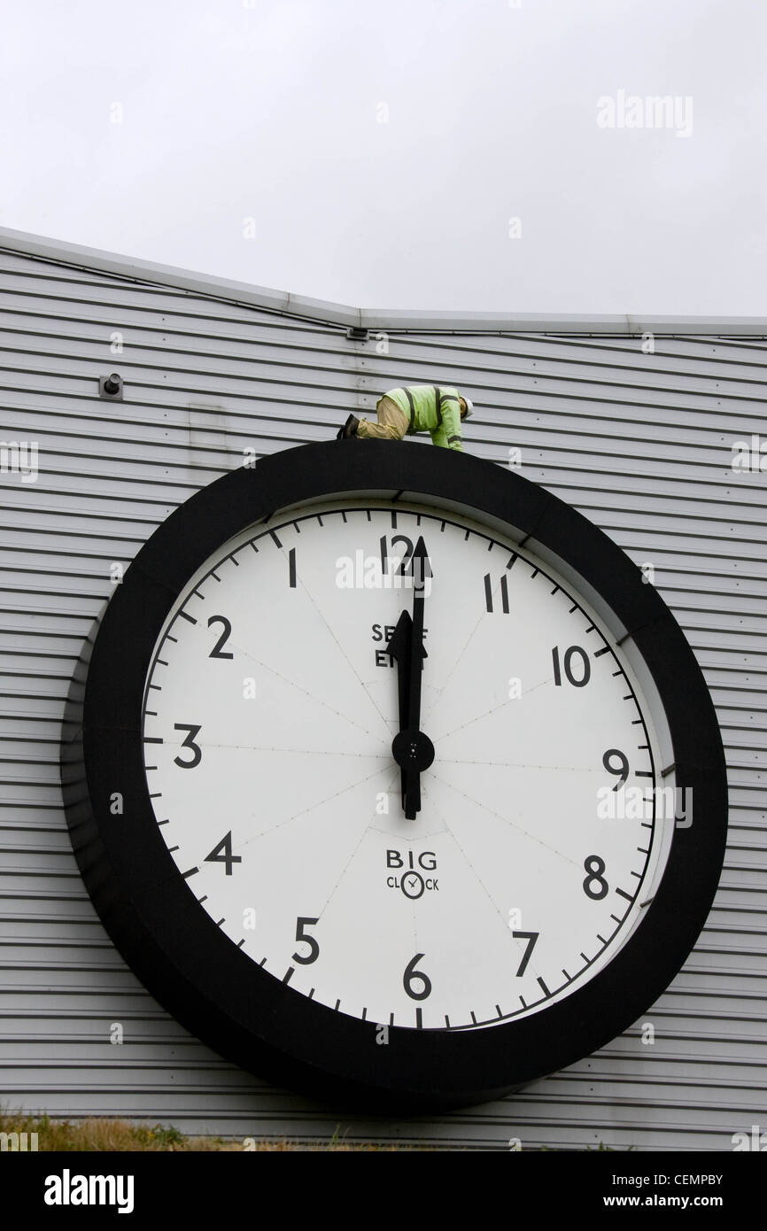 Model figure on top of a giant clock on the side of an industrial building Stock Photo