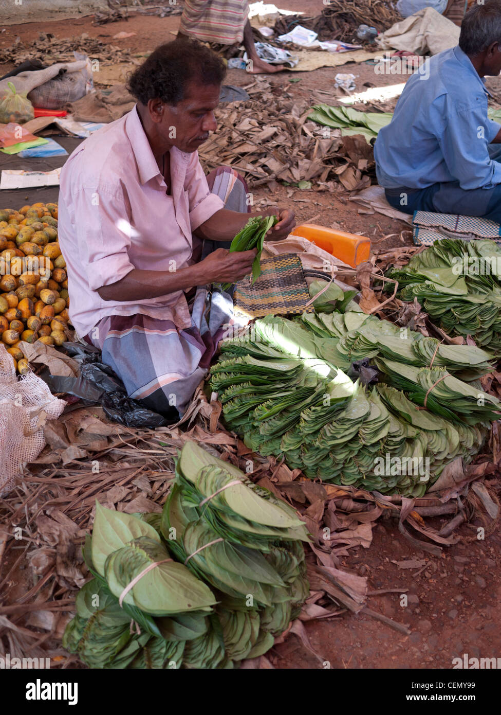 A betel nut seller arranges leaves for a stall display sitting on the