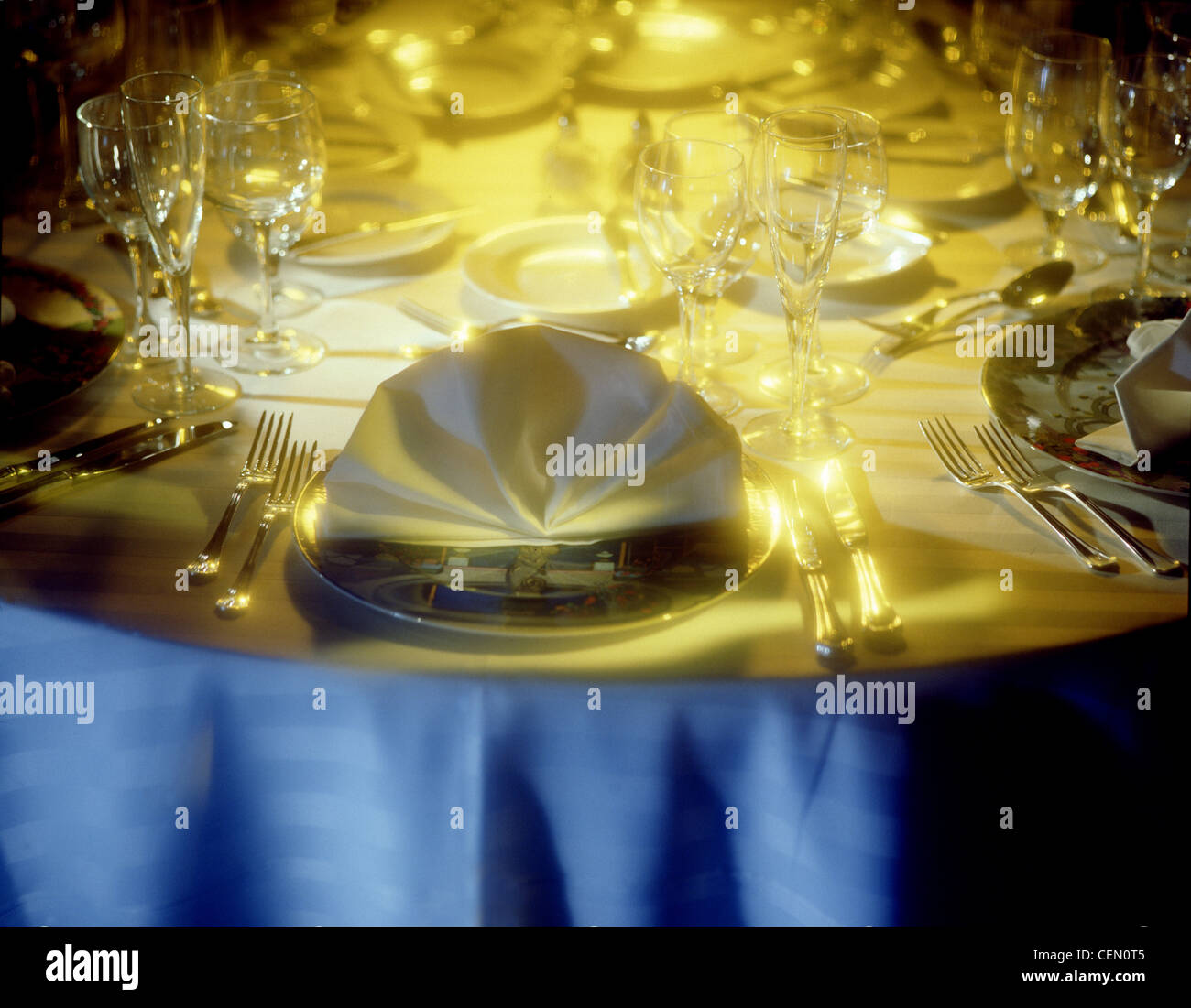 Banquet table setting with dramatic light.  Plate with fanned napkin is center of frame. Empty plates, no food. Stock Photo