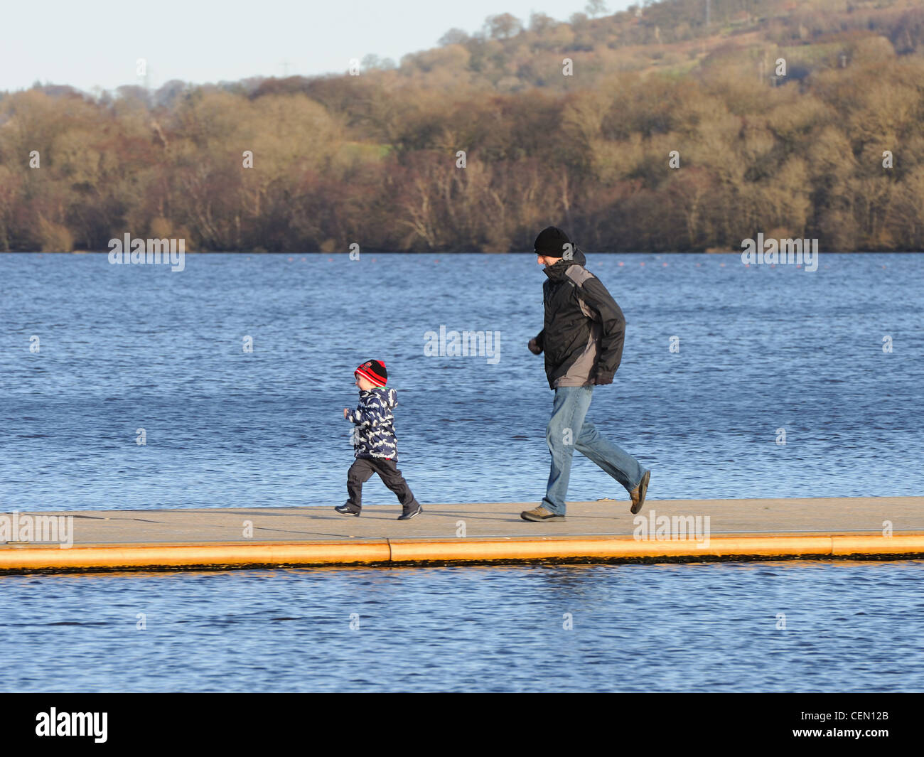 A man and boy have fun running on a pontoon on Castle Semple Loch, Clyde Muirshiel Regional Park Stock Photo