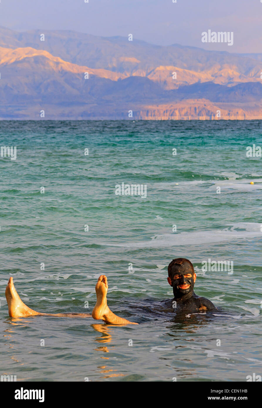 Bather floats in the super salty waters of the Dead Sea in Israel after covering himself with mineral rich mud. Stock Photo
