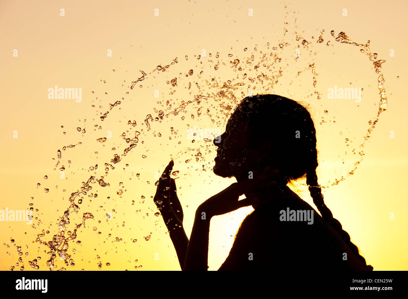 Indian girl splashing water over herself at sunset. Silhouette. India Stock Photo