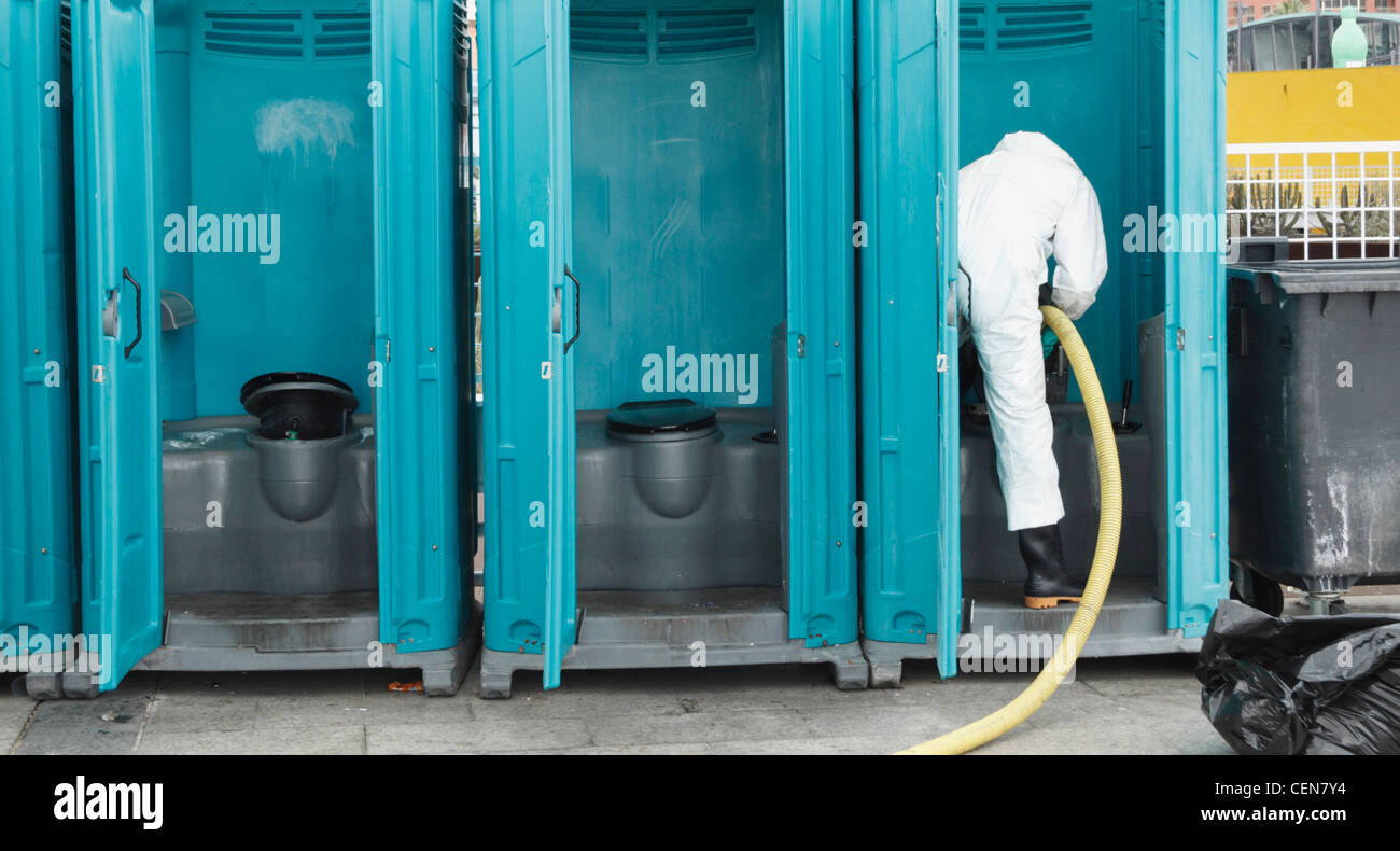 Worker emptying and cleaning portaloo chemical toilets at carnival Stock