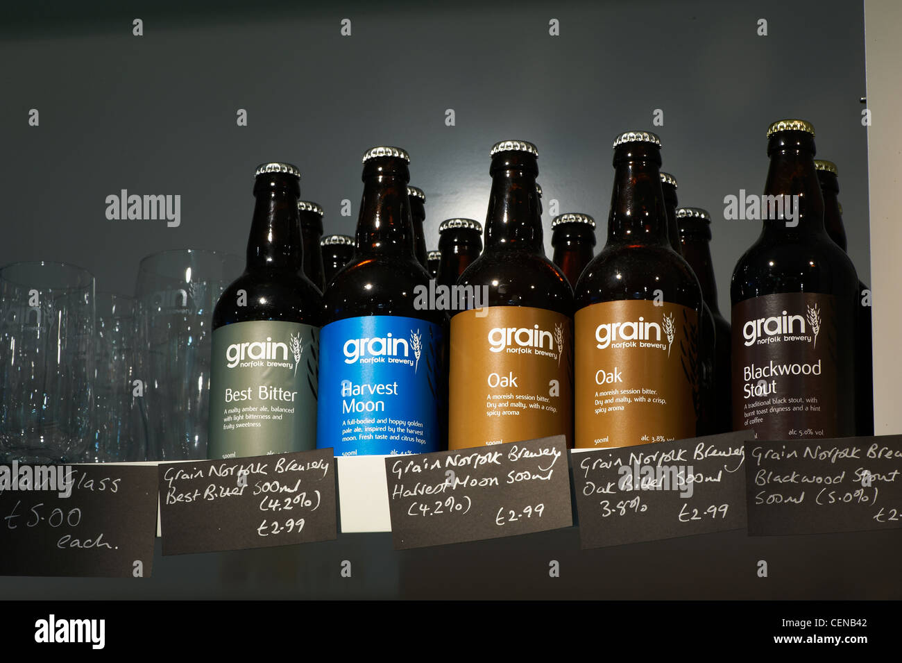 Close up of bottles of beer for sale on a shelf, showing some glasses and price labels. Stock Photo