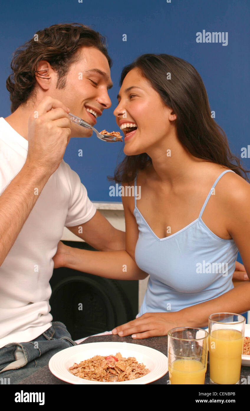 Couple having breakfast in kitchen Semi profile of female long brunette hair wearing pale blue vest top looking at boyfriend Stock Photo