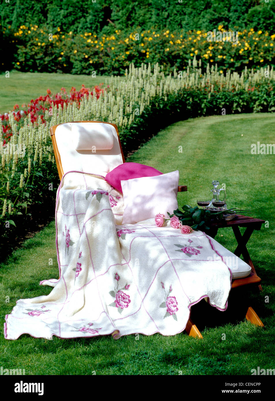 Wood sunlounger white cushion, headrest, and pink and white small cushions, draped white blanket embroidered pink squares and Stock Photo
