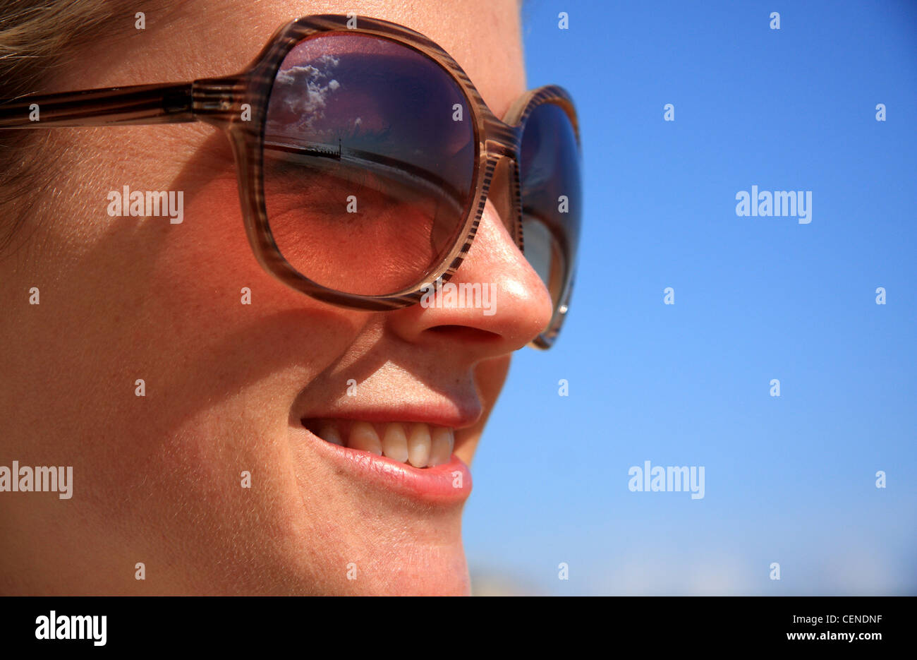 Female wearing sunglasses, smiling against the blue sky Stock Photo Alamy