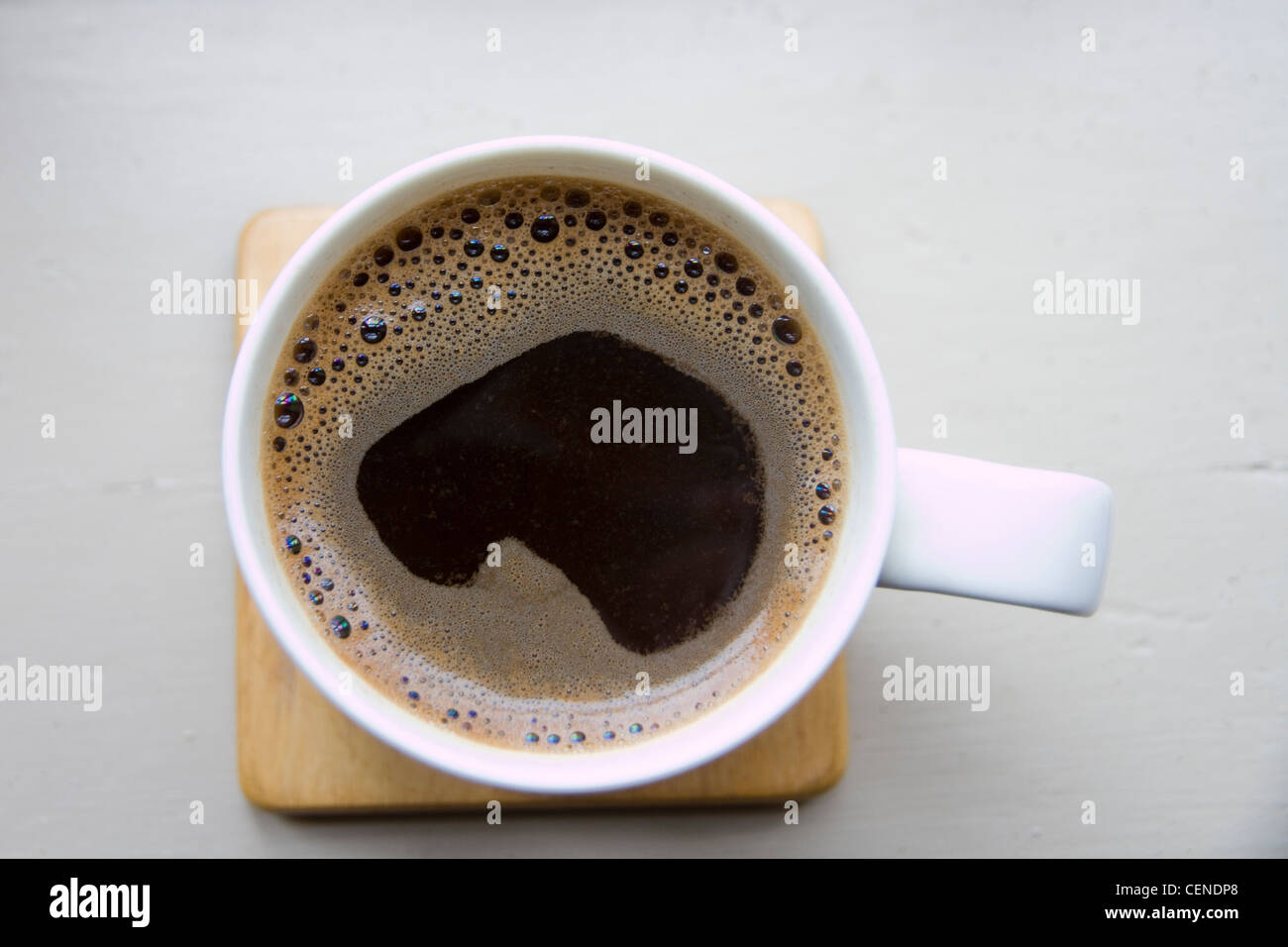 A mug of black coffee on a square wooden coaster on a white-painted surface Stock Photo