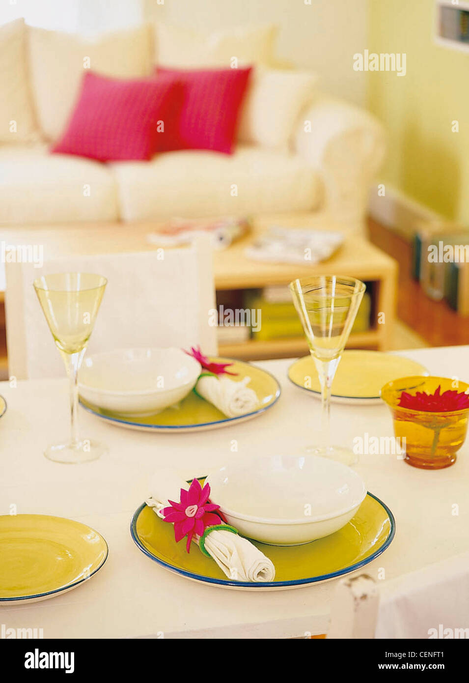 Easy Living Table white tablecloth laid green plates blue rim, white napkins red flower napkin rings, white bowls, yellow Stock Photo