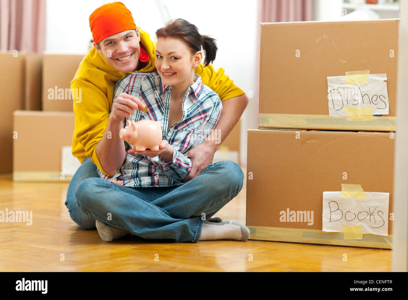 Young couple among boxes putting coin in piggy bank Stock Photo - Alamy