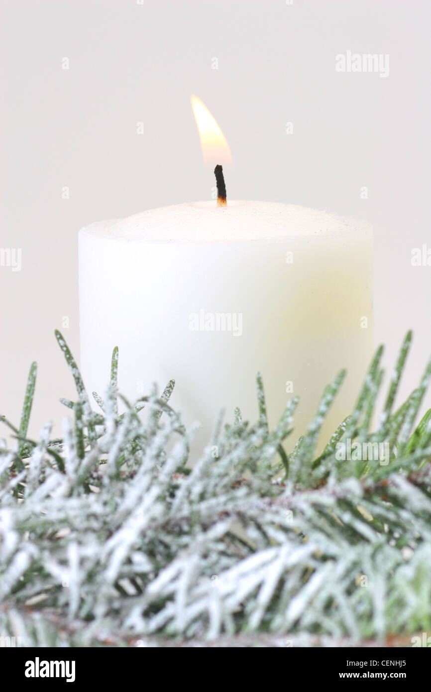 A white pillar candle in a wreath made from fake snow covered pine