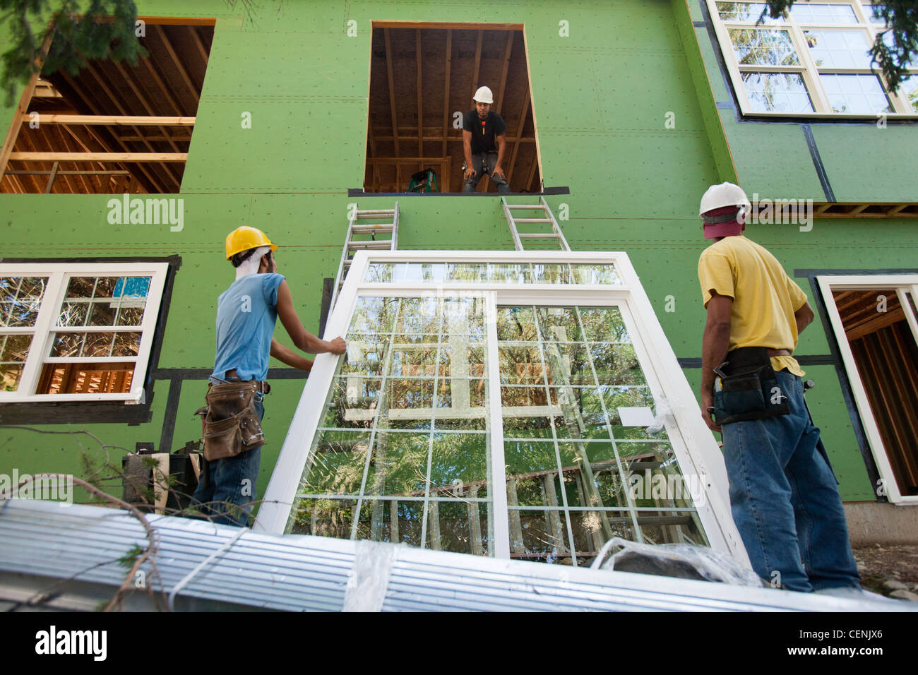 Hispanic Carpenters Preparing To Hoist Window Frame To Second