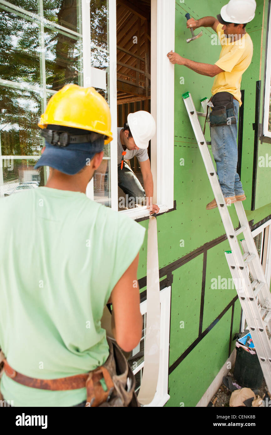 Hispanic carpenters nailing and installing flashing around window frame
