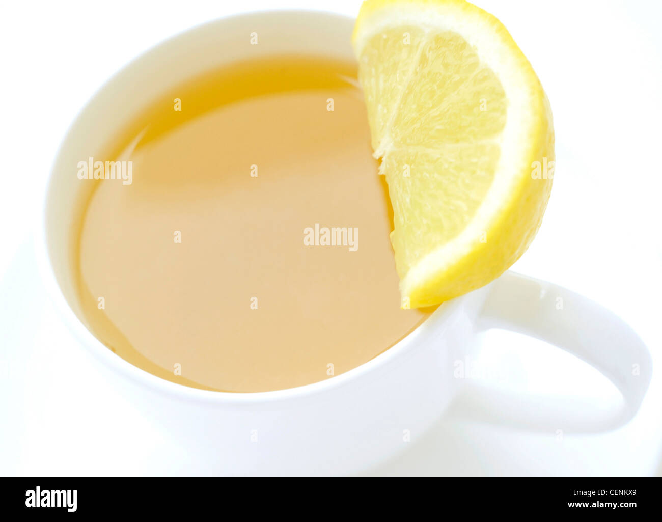 A close up of a white cup and saucer filled with a yellow fruit tea, with a slice of lemon on one side of the cup Stock Photo