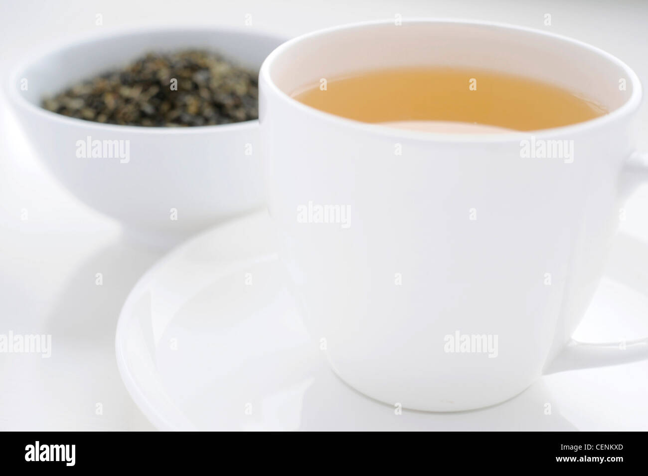 A close up of a white cup and saucer filled with a yellow fruit tea, with a bowl of loose tea in the background Stock Photo