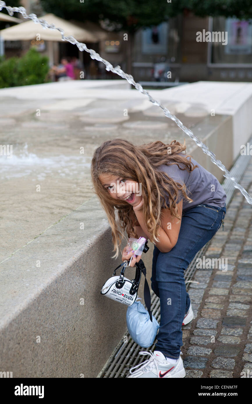 Young girl with long curly hair passing under a fountain water spring Stock Photo