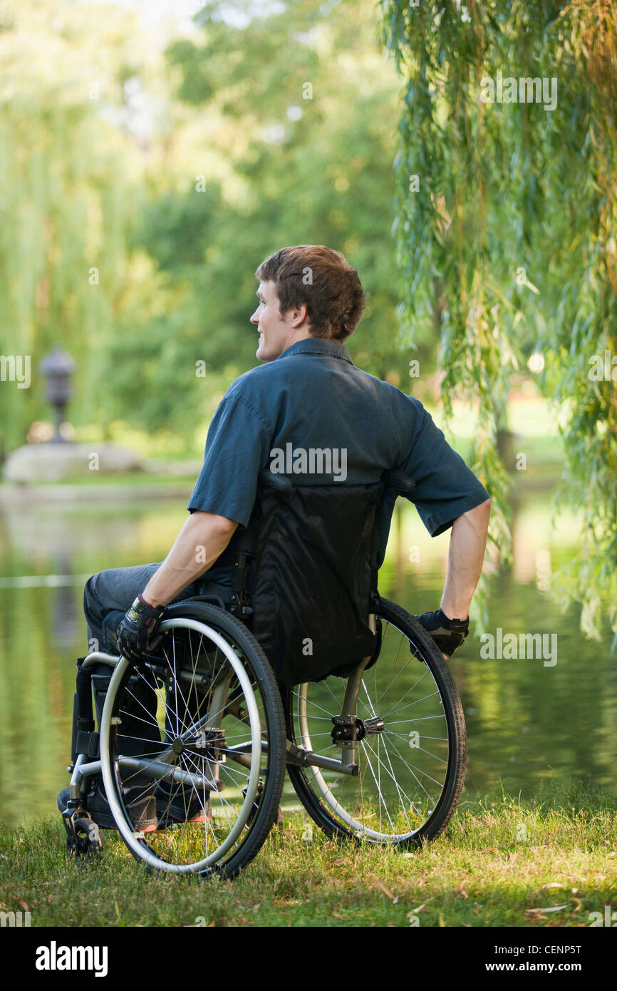 Man with spinal cord injury in a wheelchair in wheelchair enjoying at the pond side in public park Stock Photo