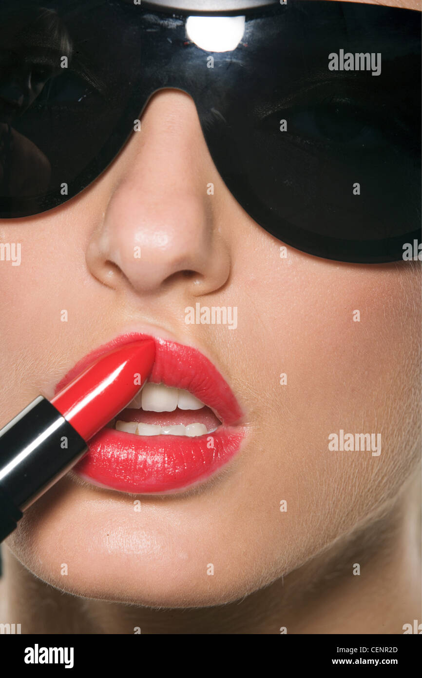 Female wearing bright red lipstick and large black sunglasses, applying