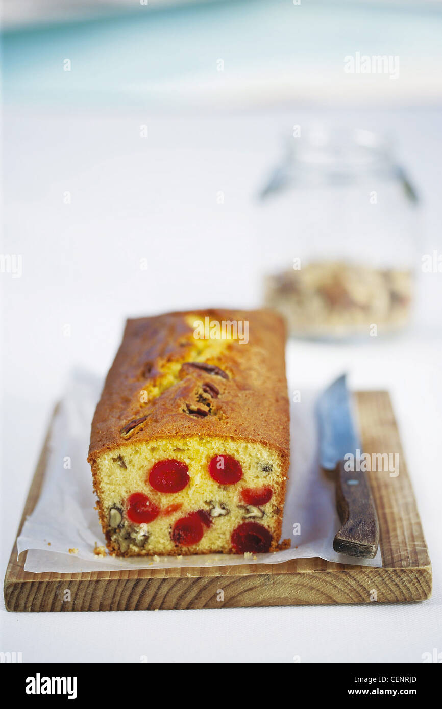 Cherry and nut loaf cake on wax paper with wooden handled knife on wooden chopping board Stock Photo