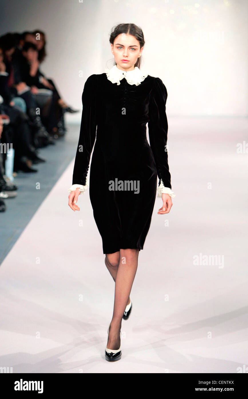 Black velvet long sleeved knee length dress with white frilly trimming, monochrome court shoes Stock Photo
