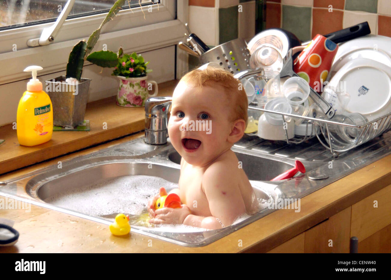 Female Child Sitting In Kitchen Sink Full Of Soapy Water