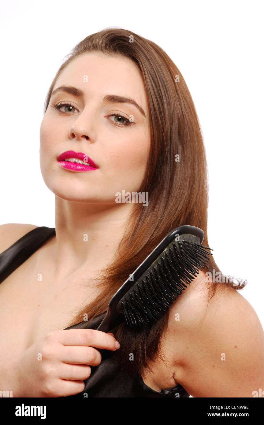 Female wearing bright pink lipgloss and black satin dress brushing long straight brunette hair brush looking to camera mouth Stock Photo