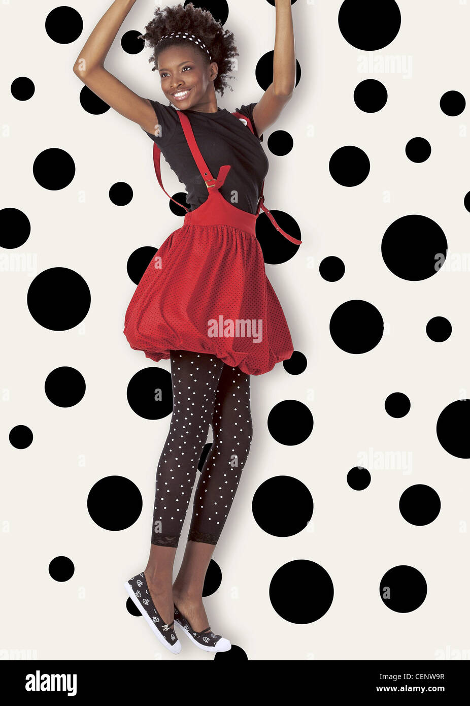 Female wearing black and white polka dot leggings, black T shirt, red puffball dress Stock Photo
