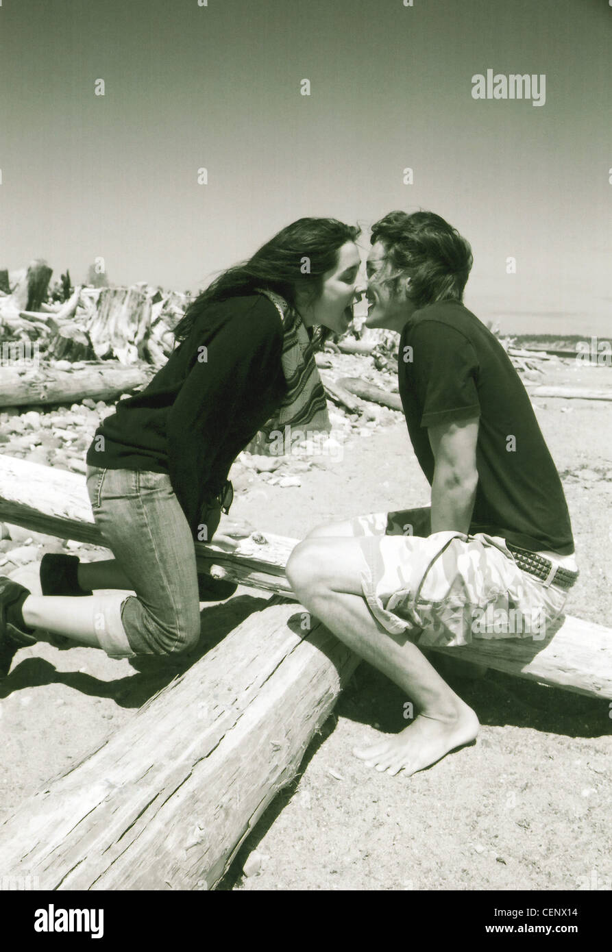 Black and white image of male and female sitting on wooden seesaw on beach leaning towards each other about to kiss Stock Photo
