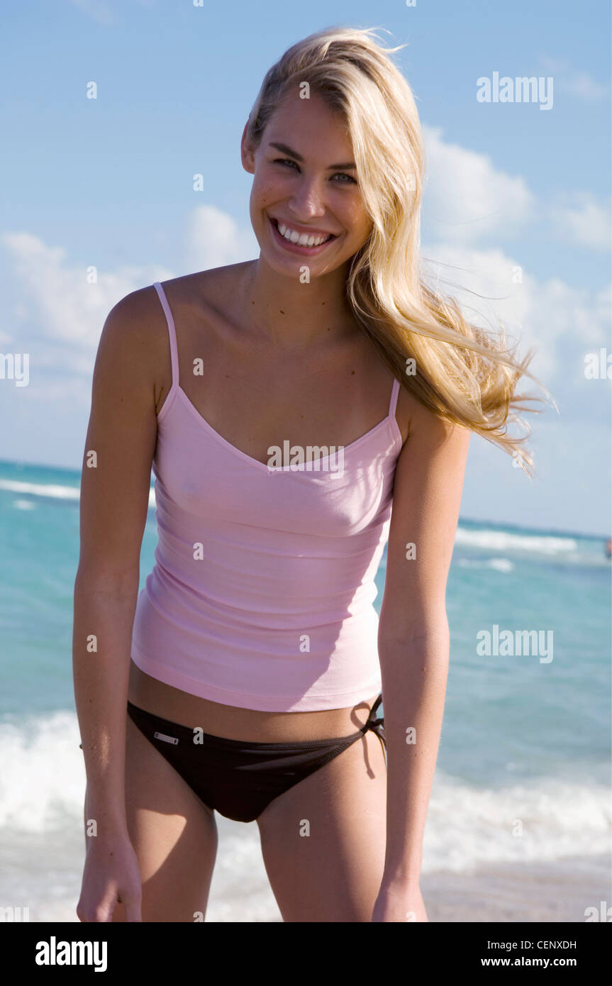 Female very long blonde hair wearing pink vest top and brown bikini bottoms leaning slightly forward hands on thighs looking Stock Photo