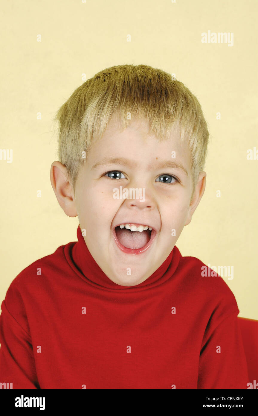 Blonde three year old boy wearing red turtle neck jumper smiling big at the camera Baba and Kleuter Stock Photo