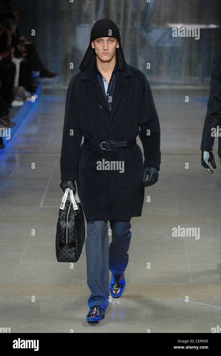 Woolly hat, belted knee length coat, Louis Vuitton briefcase and reflective  blue sneakers, with black leather gloves Stock Photo - Alamy