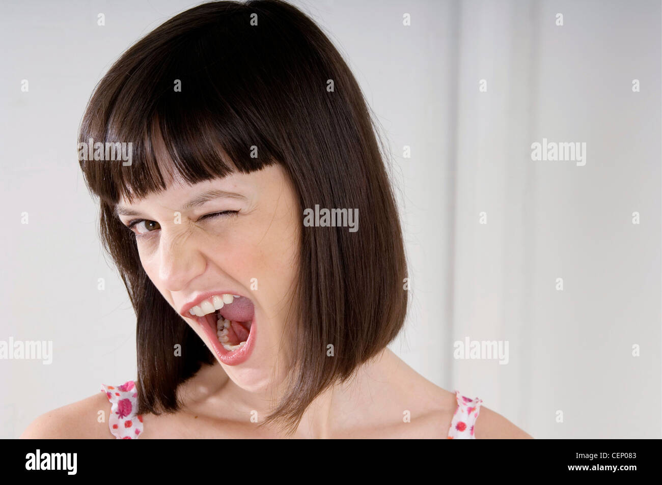 Female with brunette hair head titled sideways looking to camera winking mouth wide open showing teeth  RBO Stock Photo