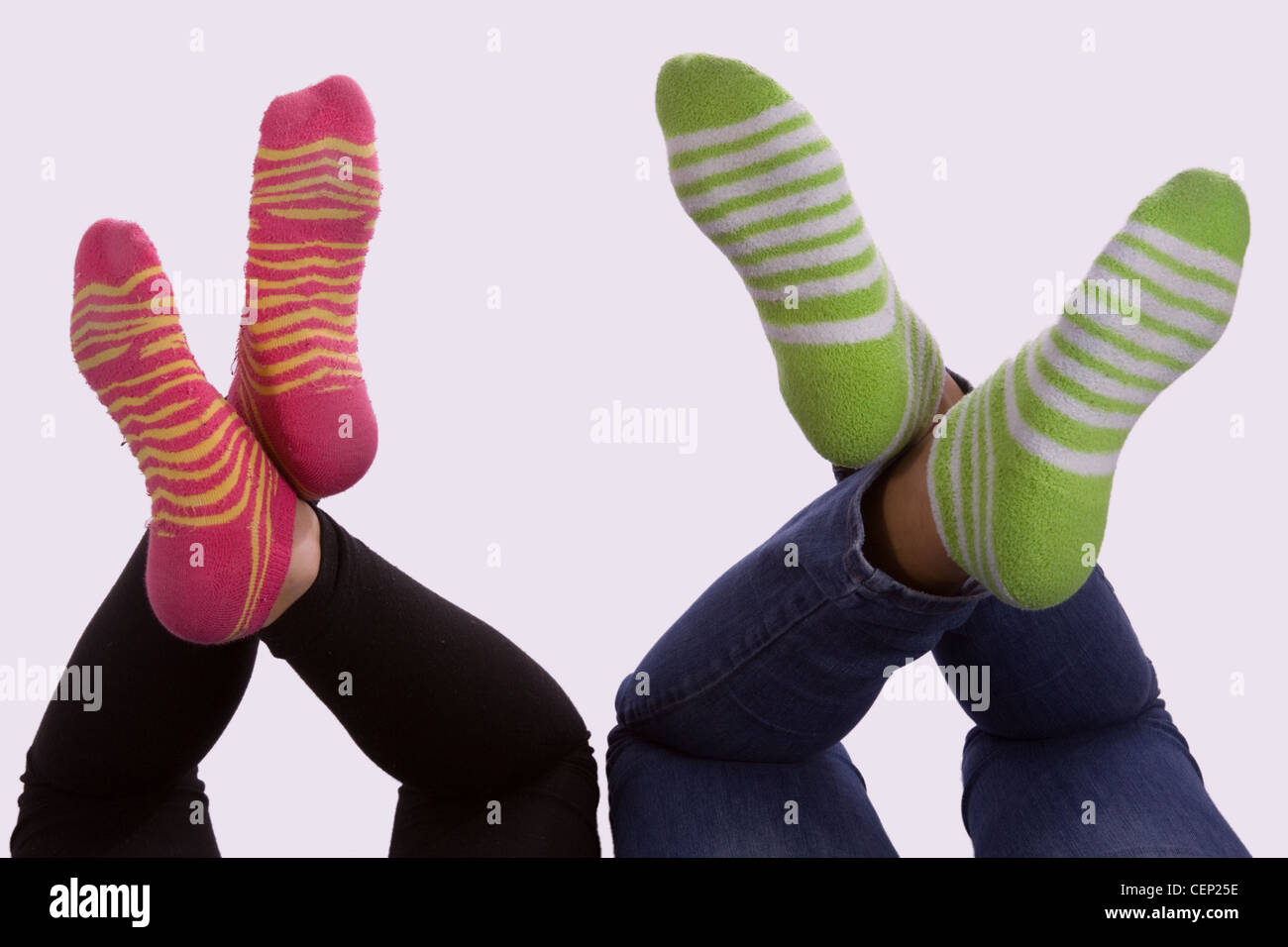 legs of two young girls feet wearing striped socks green and pink with legs  crossed Stock Photo - Alamy