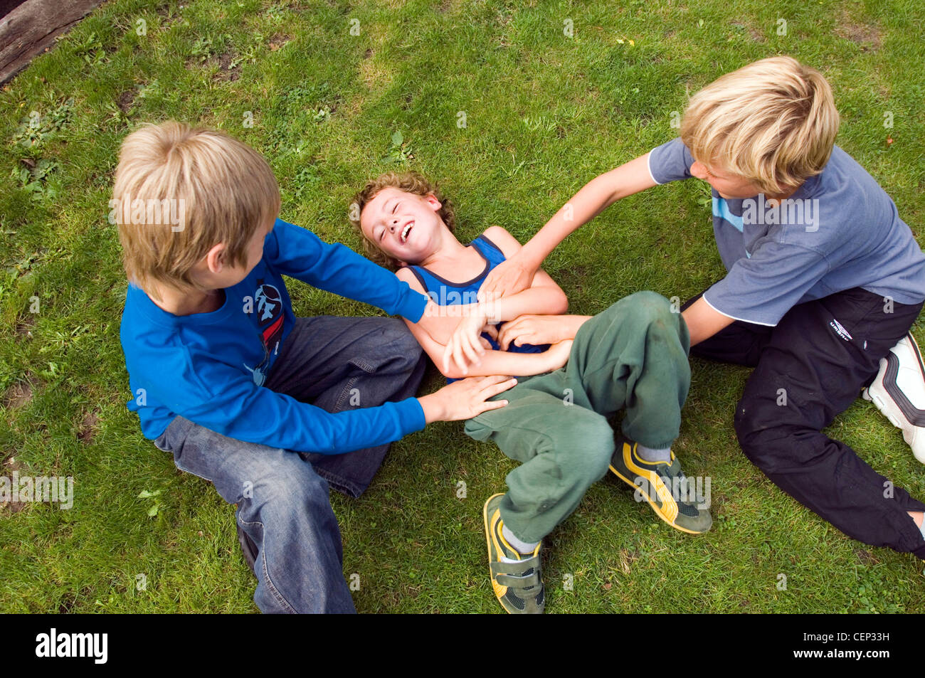 Two male children tickling another male child Stock Photo Alamy