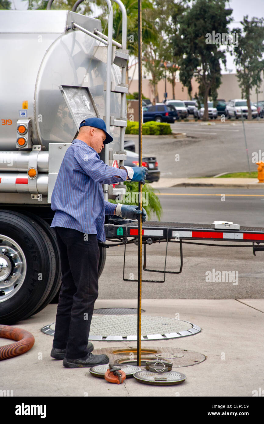Using a long dip stick, a gasoline delivery man measures the levels in a service station's underground storage tanks. Stock Photo