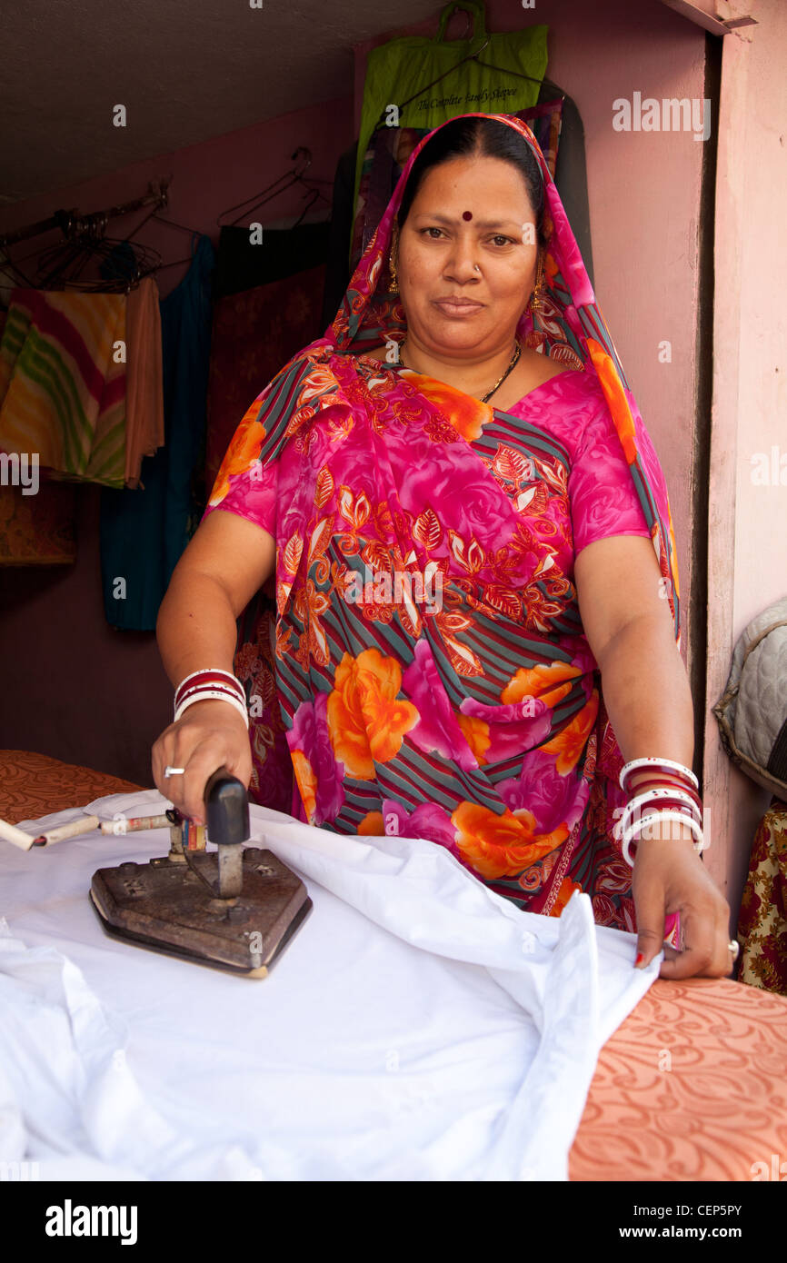 Smiling Hindu woman in bright floral sari ironing clothes Stock Photo