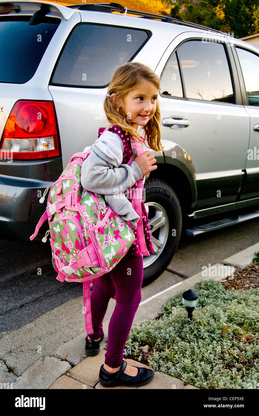 Carrying her backpack and lunch box, a 6 year old girl waits by the car to go to school in San Juan Capistrano CA. Model Release Stock Photo