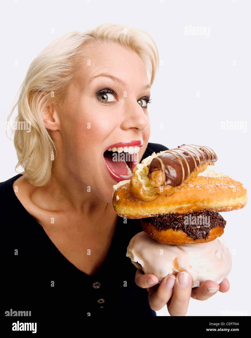 Female holding an iced bun, a chocolate donut, a sugared donut and a chocolate eclair piled up about to take a bite Stock Photo