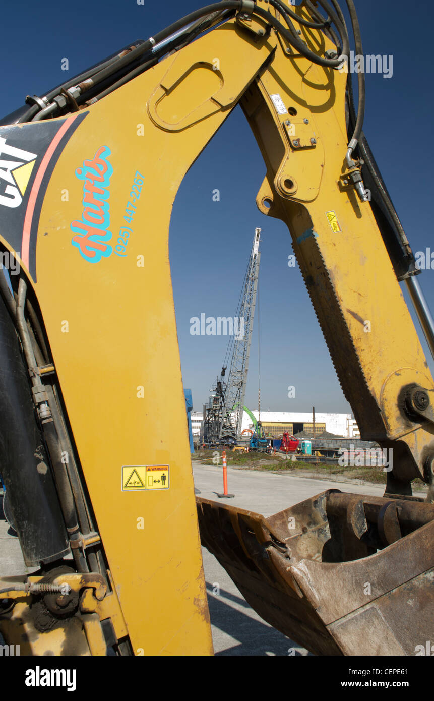 Yellow CAT backhoe arm and bucket framing a crane dredge barge in the background. Stock Photo