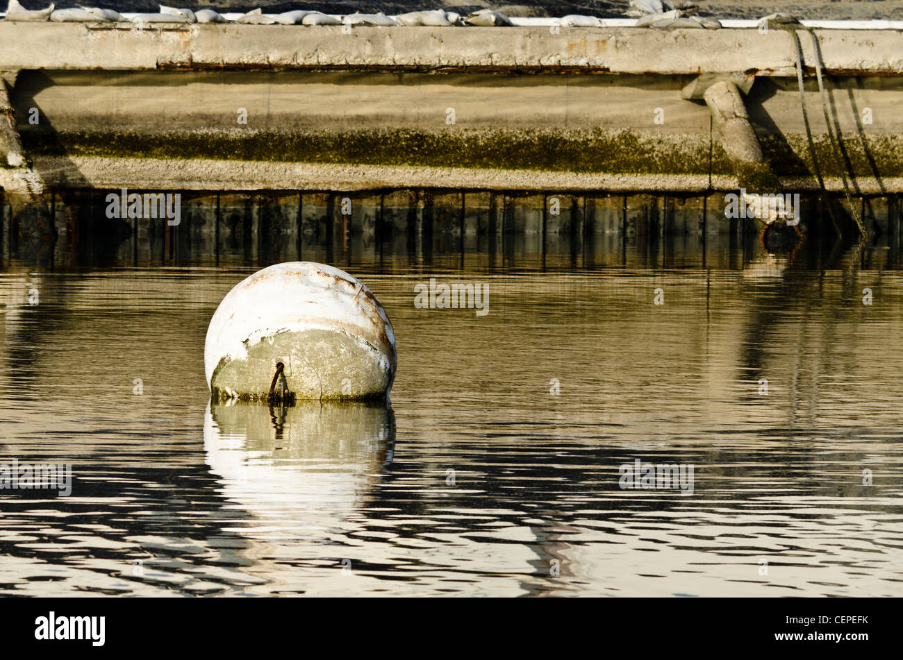 White buoy in the water with a seawall in the background Stock Photo