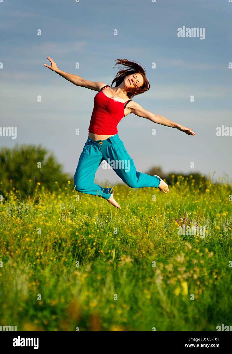 Happy young woman in sport wear jumping on a sunset field Stock Photo ...