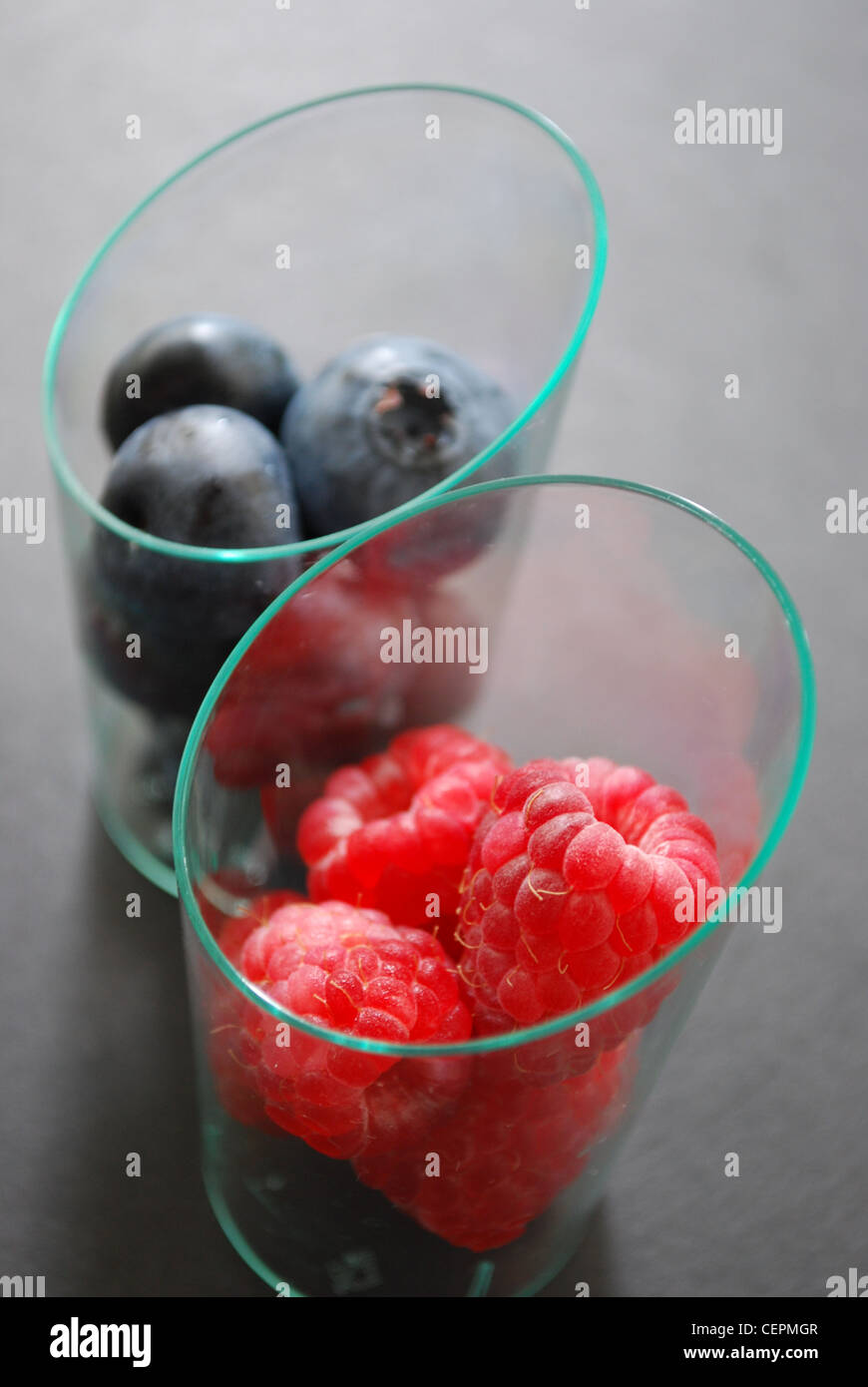 Blueberry Raspberry Size Comparison Closeup of blueberries and raspberries in transparent glasses on dark ...