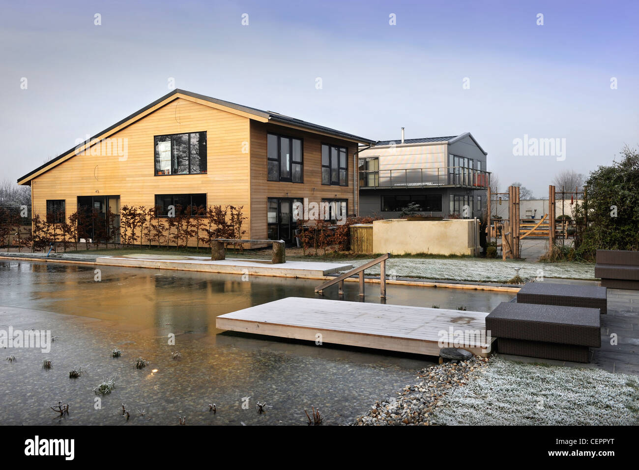 A natural swimming pool which has iced over in winter at a self build wooden clad home UK Stock Photo