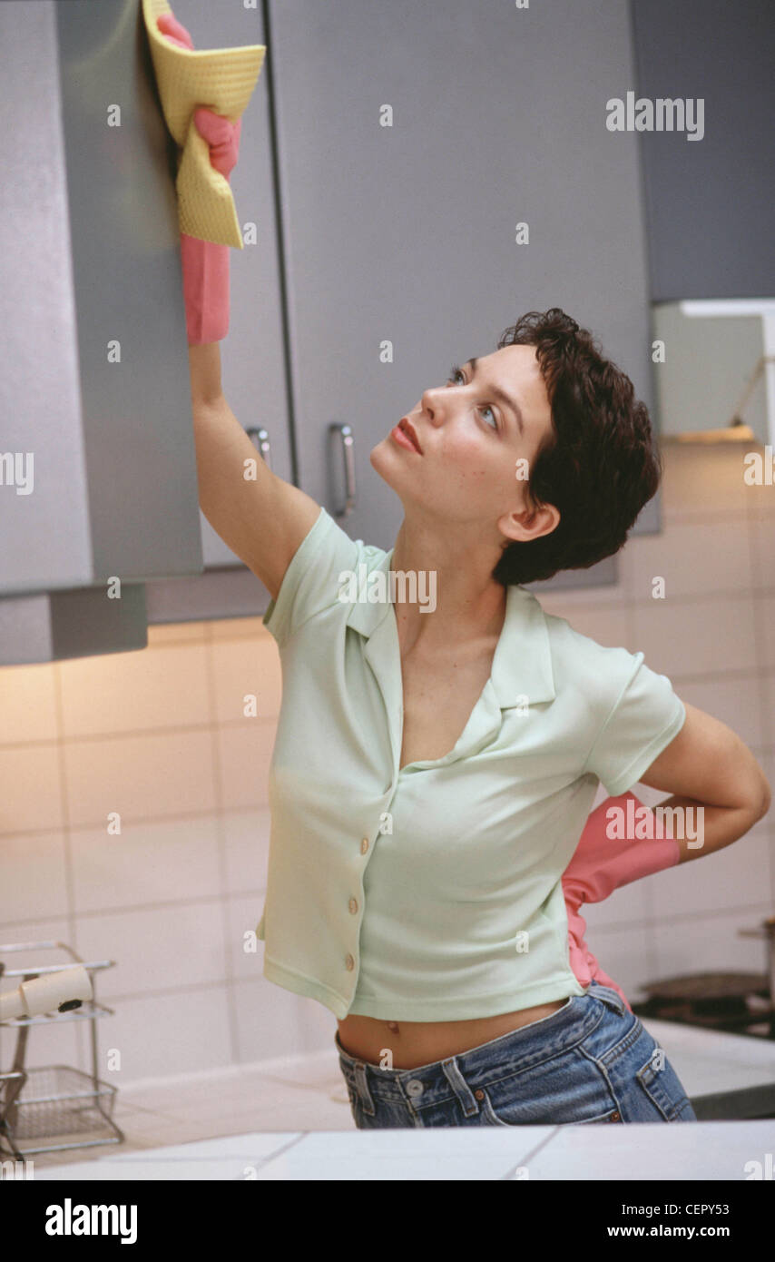 Semi profile of female short brunette hair wearing red lipstick pale green blouse blue jeans and pink rubber gloves washing Stock Photo