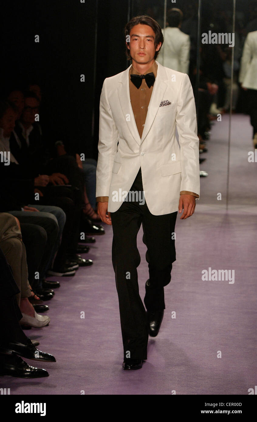 Menswear fashion show Model dark hair wearing brown shirt under white jacket  black bow tie black trousers black shoes and Stock Photo - Alamy