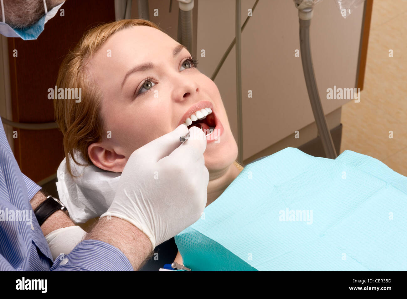 Young blond Caucasian female opening her mouth while unidentifiable dentist in white latex gloves check condition of her teeth Stock Photo